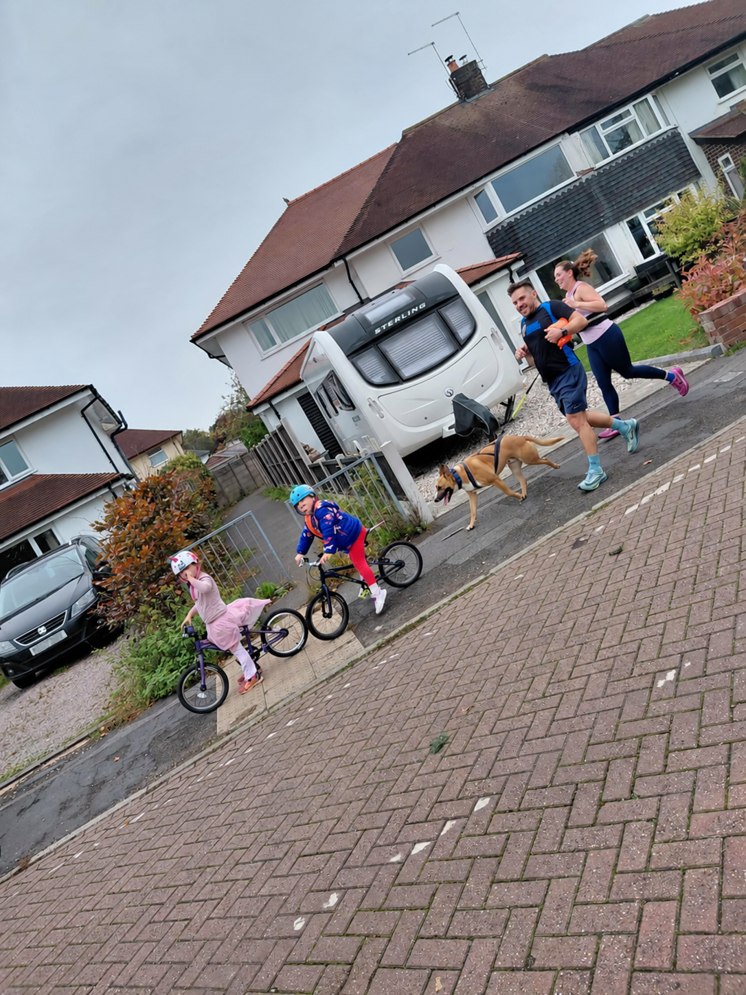 A family moving together with children cycling and adults running on a neighbourhood route