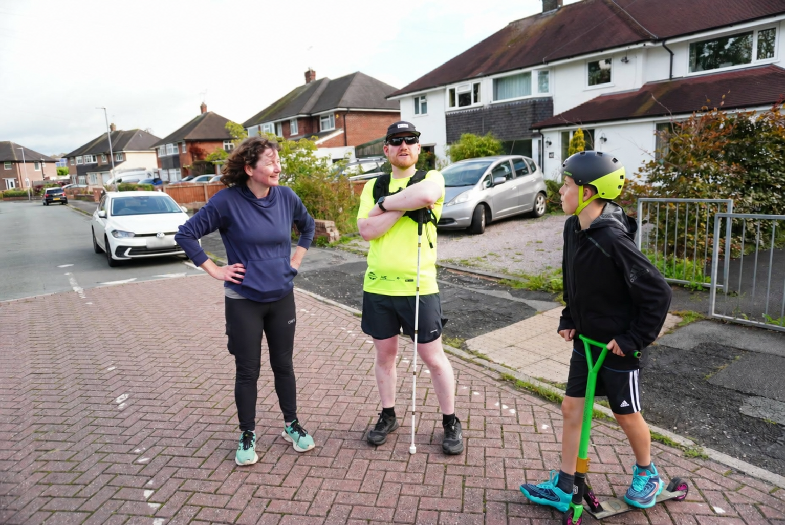 An adult and a young person with a scooter talking with a Dash participant on a neighbourhood street